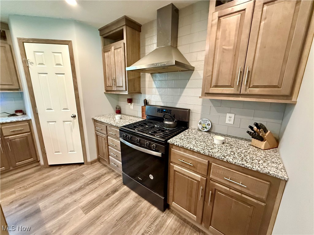 2306 Gordon Road Northwest Dover, OH 44622 - Photo 5 of 26 Kitchen with wall chimney exhaust hood, gas stove, backsplash, light wood finished floors, and light stone counters