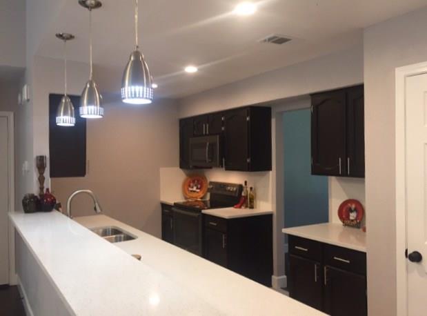3305 Spaniel Drive Austin, TX 78759 - Photo 18 of 20 A contemporary kitchen features dark cabinetry, bright white countertops, and sleek pendant lighting.