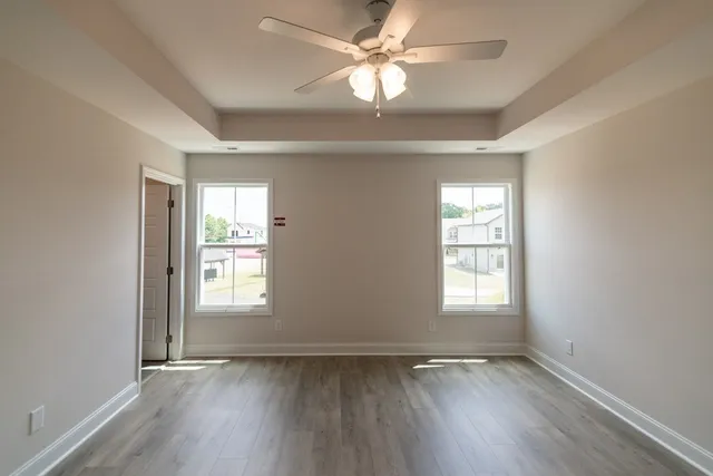 an empty room with wooden floor ceiling fan and windows