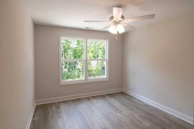 an empty room with wooden floor fan and windows