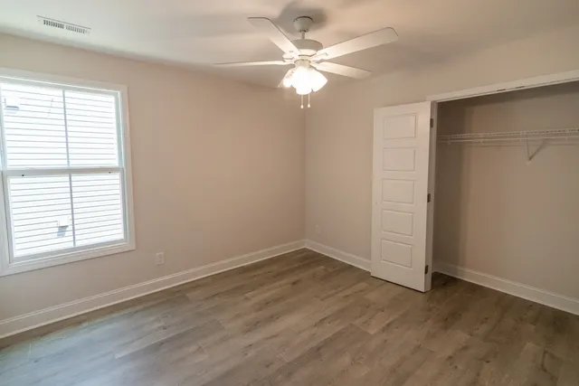 an empty room with wooden floor fan and windows