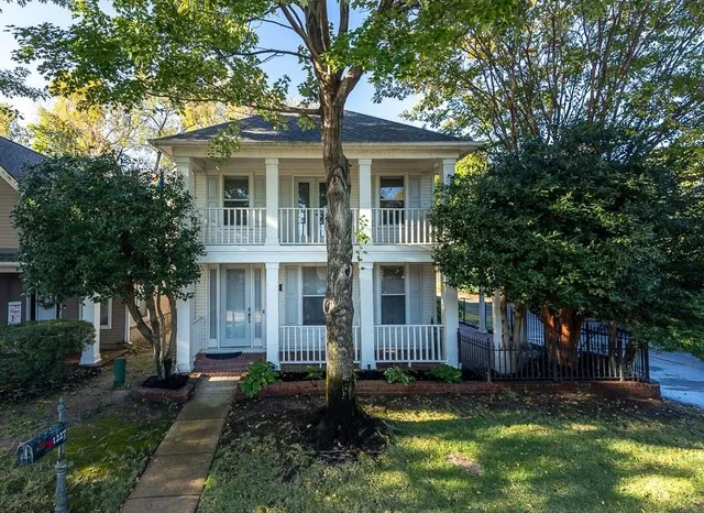 a view of a white house next to a yard with plants and trees