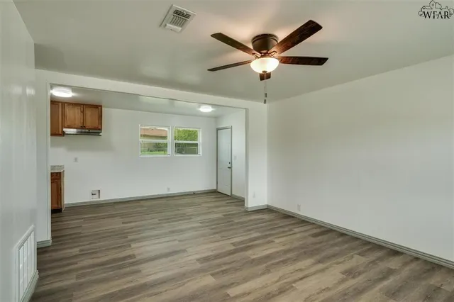 an empty room with wooden floor a ceiling fan and windows