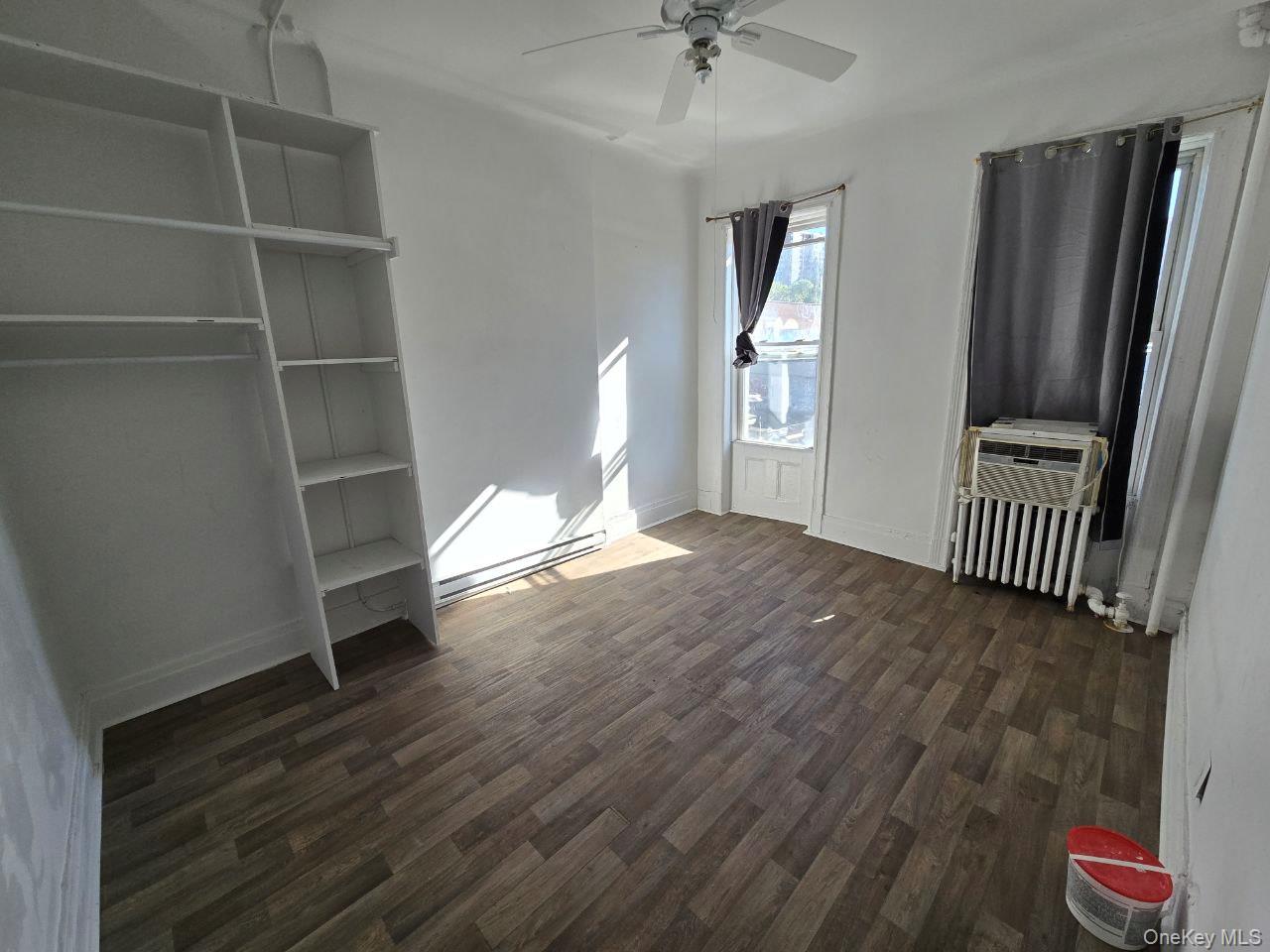 Unfurnished bedroom featuring dark wood-type flooring, radiator heating unit, a ceiling fan, a baseboard radiator, and cooling unit