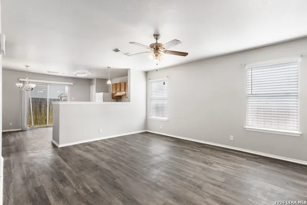 an empty room with wooden floor chandelier fan and windows