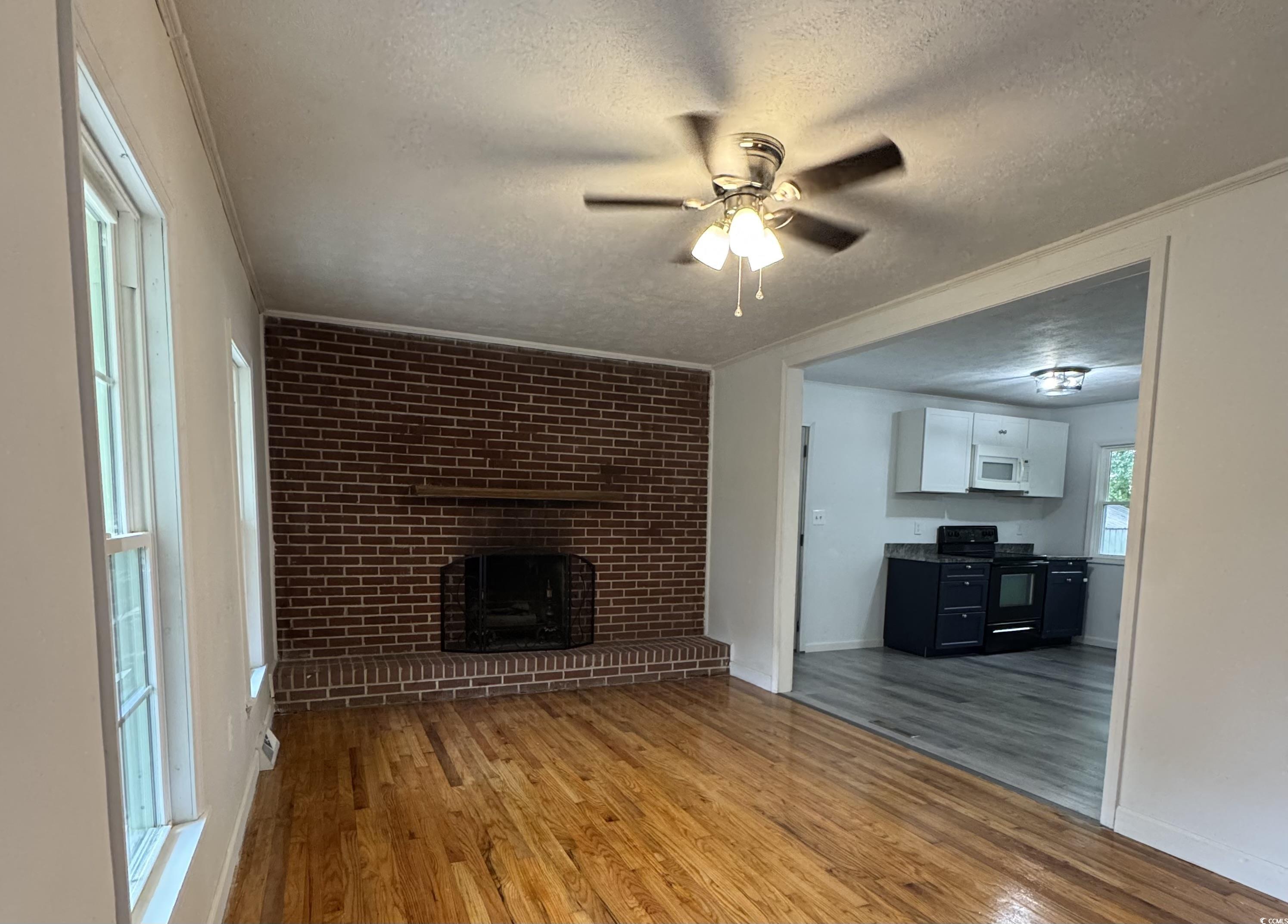 1127 State Rd S-17-640 Dillon, SC 29536 - Photo 10 of 26 Unfurnished living room with light wood finished floors, a fireplace, a textured ceiling, ceiling fan, and crown molding