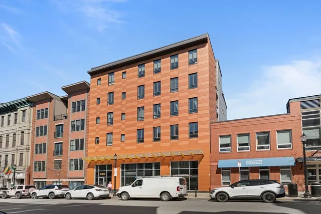 a front view of a building with lot of cars and trees