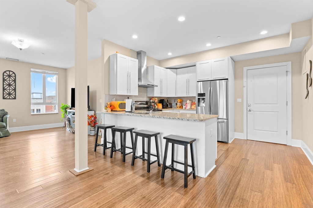 380 West Broadway, Unit 401 Boston, MA 02127 - Photo 5 of 25 a kitchen with stainless steel appliances granite countertop a refrigerator a stove top oven and a dining table with wooden floor