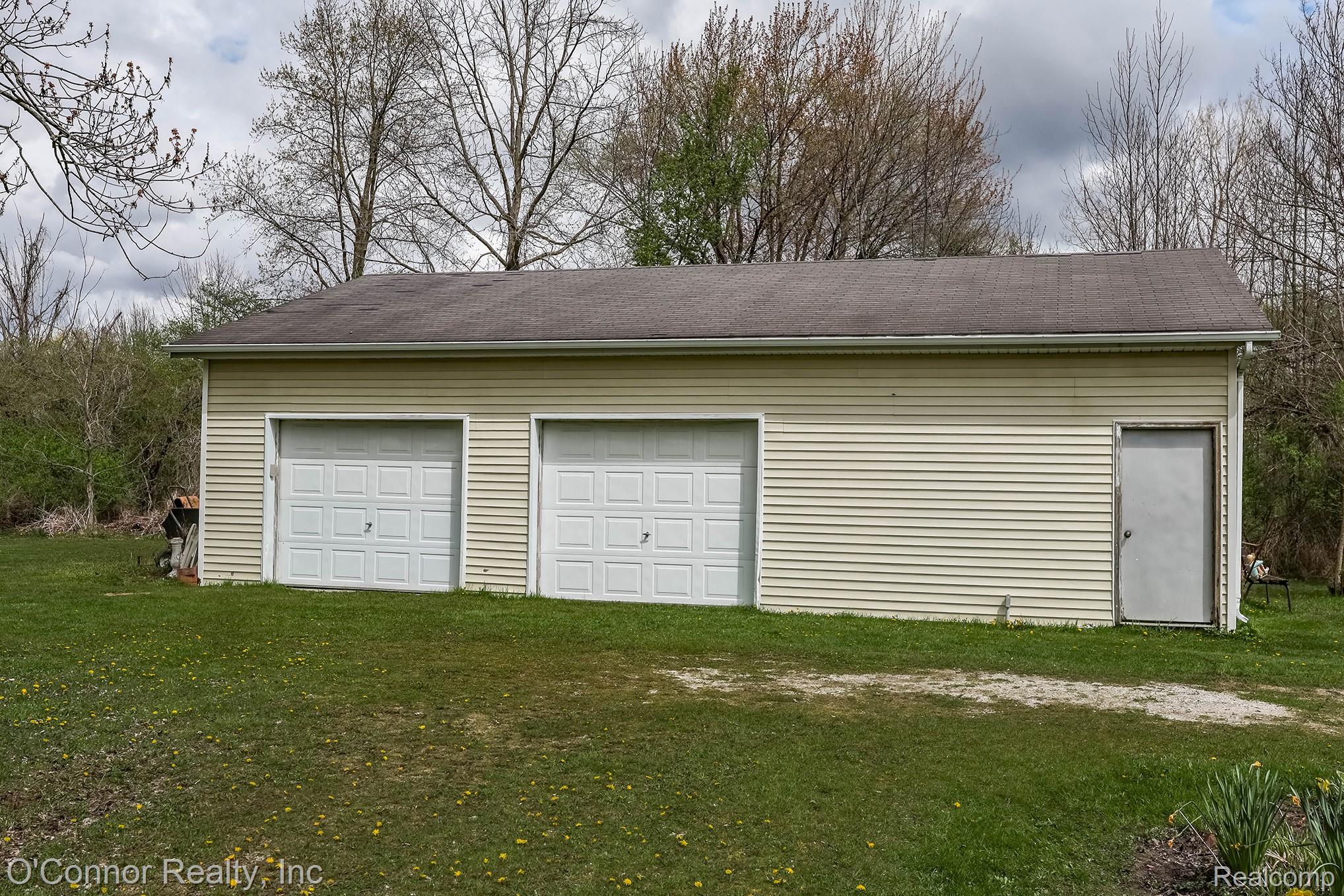 3323 Kinney Road Emmett, MI 48022 - Photo 20 of 29 Detached garage structure featuring light-colored siding, a dark shingle roof, two white panel garage doors, and a side entry door
