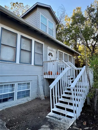 a view of a house with wooden deck stairs and a large tree