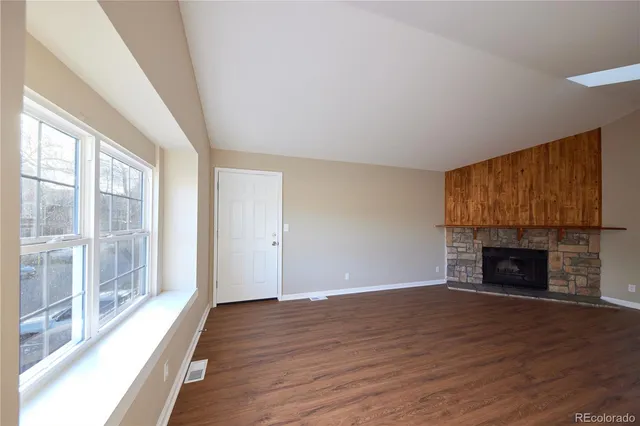 a view of an empty room with wooden floor fireplace and a window