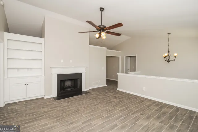 a view of a livingroom with a fireplace a ceiling fan and kitchen space