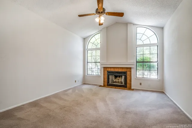 an empty room with windows fireplace and fan