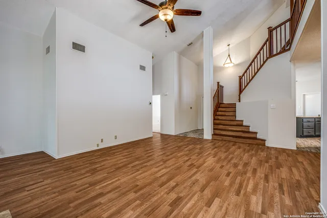 a view of an empty room with wooden floor and a ceiling fan