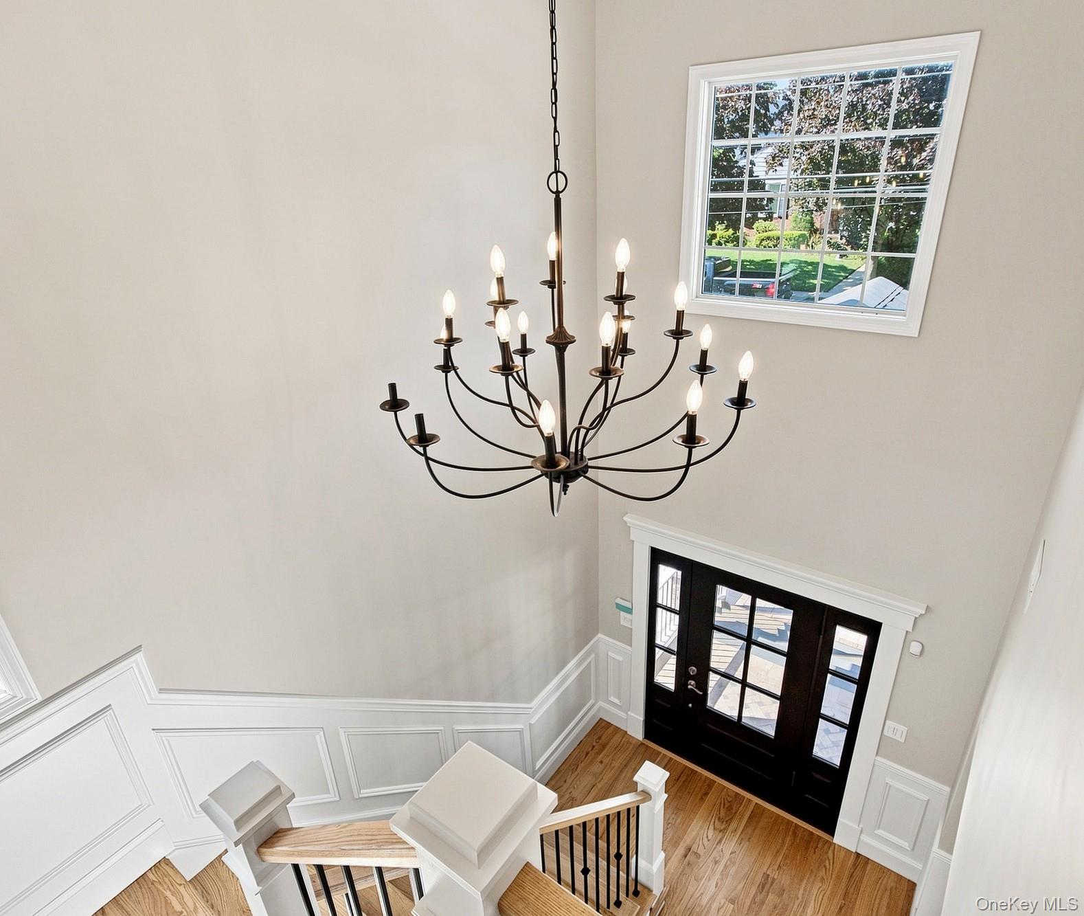 148 Latham Road Mineola, NY 11501 - Photo 3 of 27 Spacious foyer featuring a multi-tier chandelier, wood-finish flooring, white panel molding, and a dark-toned entry door with multiple glass panes.