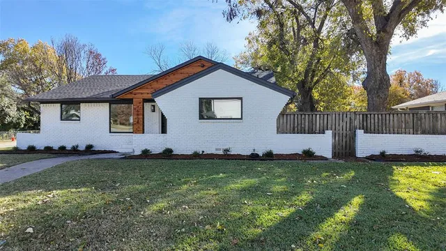 a house that is sitting in the grass with large trees and wooden fence