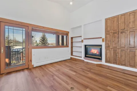 a view of an empty room with wooden floor fireplace and a window