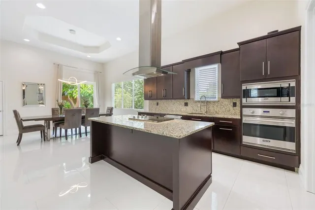 a kitchen with stainless steel appliances kitchen island granite countertop a stove top oven a sink dishwasher a dining table and chairs with wooden floor