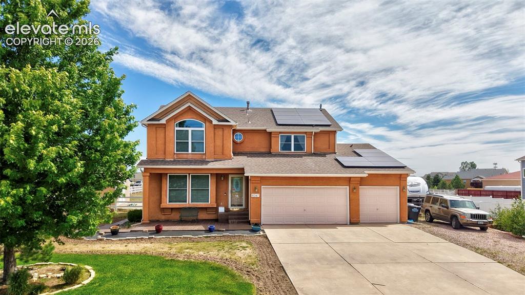 Two-story home featuring a stucco exterior, integrated solar panels, a three-car garage, and a concrete driveway