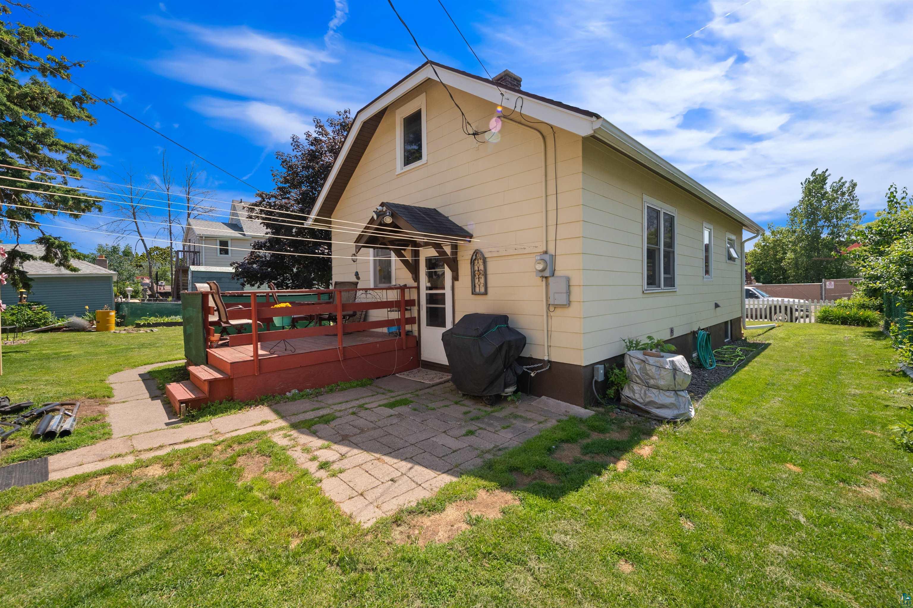 3209 Chestnut Street Duluth, MN 55806 - Photo 26 of 28 Rear exterior featuring an elevated red-stained wood deck, paver patio, side yard with mature landscaping, and white picket fencing