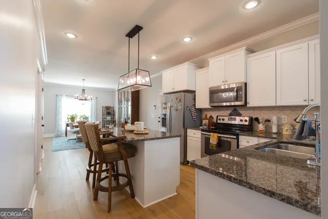 a kitchen with stainless steel appliances granite countertop a sink a stove a refrigerator cabinets and chairs