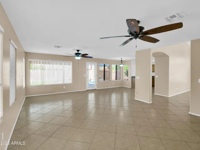 an empty room with ceiling fan and kitchen view