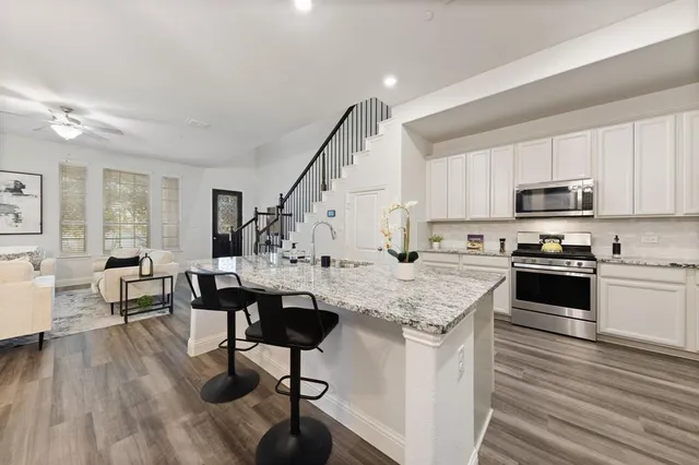 a open kitchen with granite countertop a stove top oven a sink dishwasher and white cabinets with wooden floor