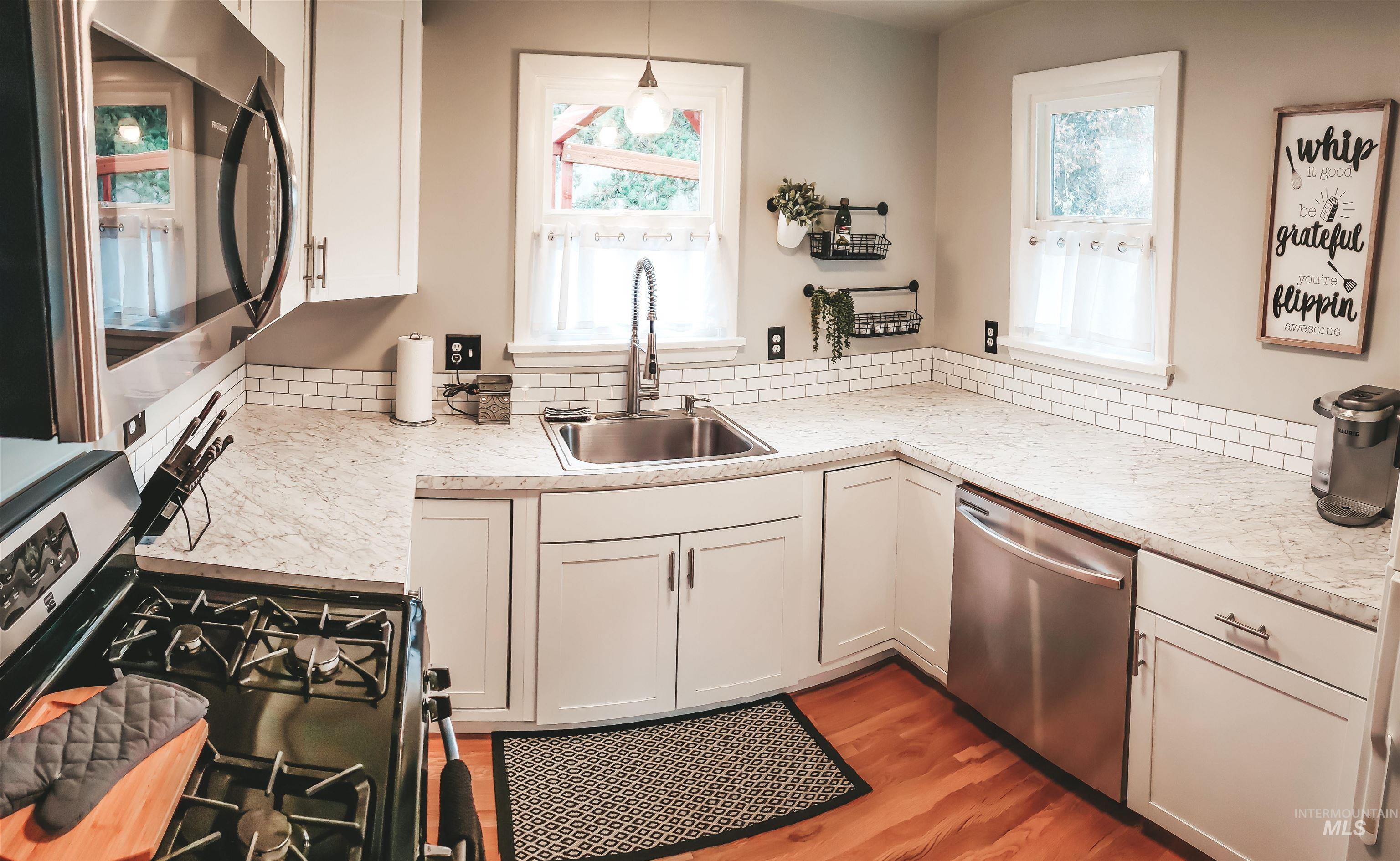 814 Baker Street Boise, ID 83706 - Photo 4 of 26 Kitchen featuring white cabinetry, light-toned countertops, a subway tile backsplash, and stainless steel appliances including a range and dishwasher