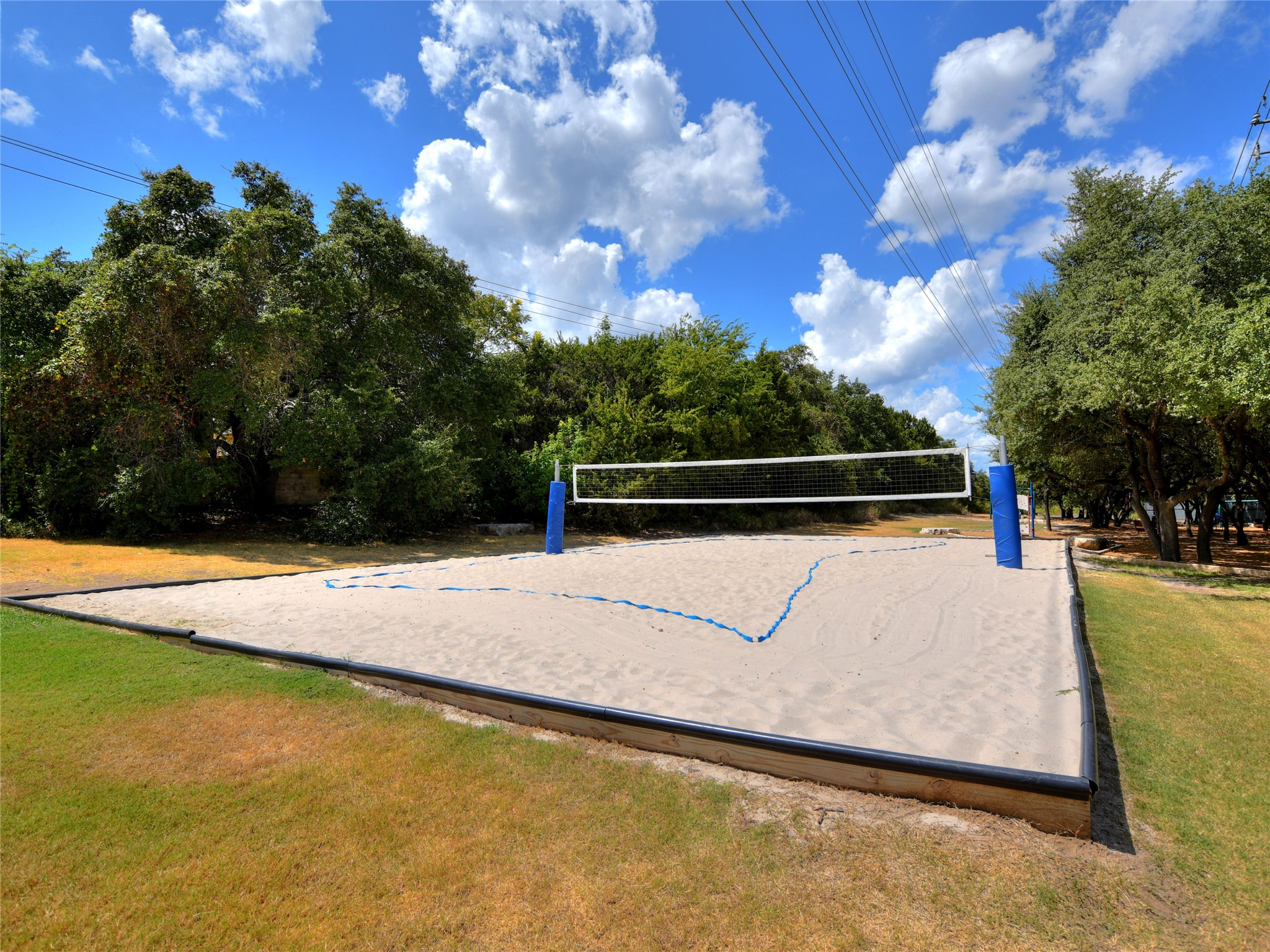2849 Grimes Ranch Road Austin, TX 78732 - Photo 36 of 37 An inviting sand volleyball court awaits under a brilliant sky, flanked by mature green trees.