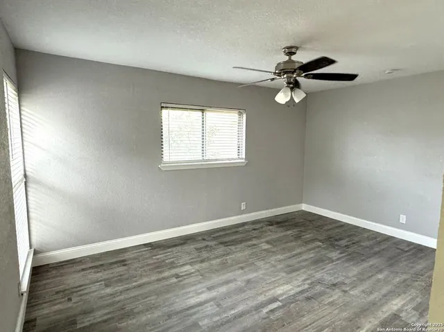 an empty room with wooden floor fan and windows