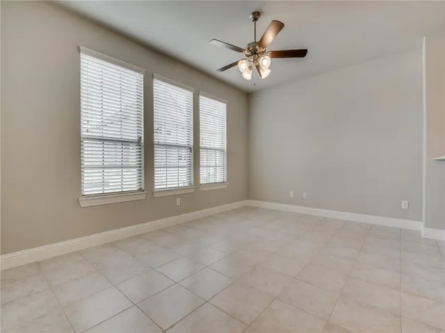 an empty room with chandelier fan and windows