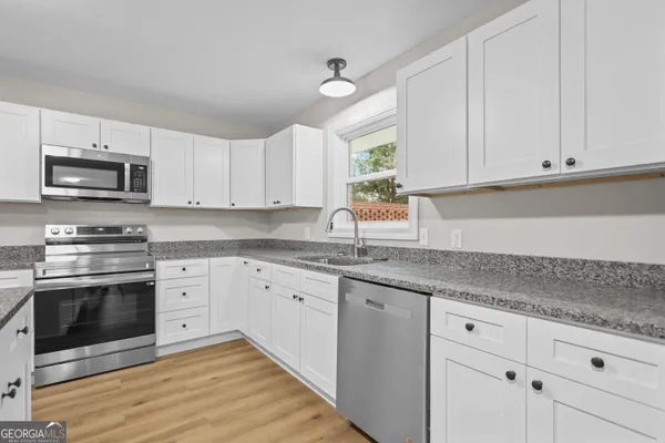 a kitchen with granite countertop white cabinets white stainless steel appliances a sink and a window