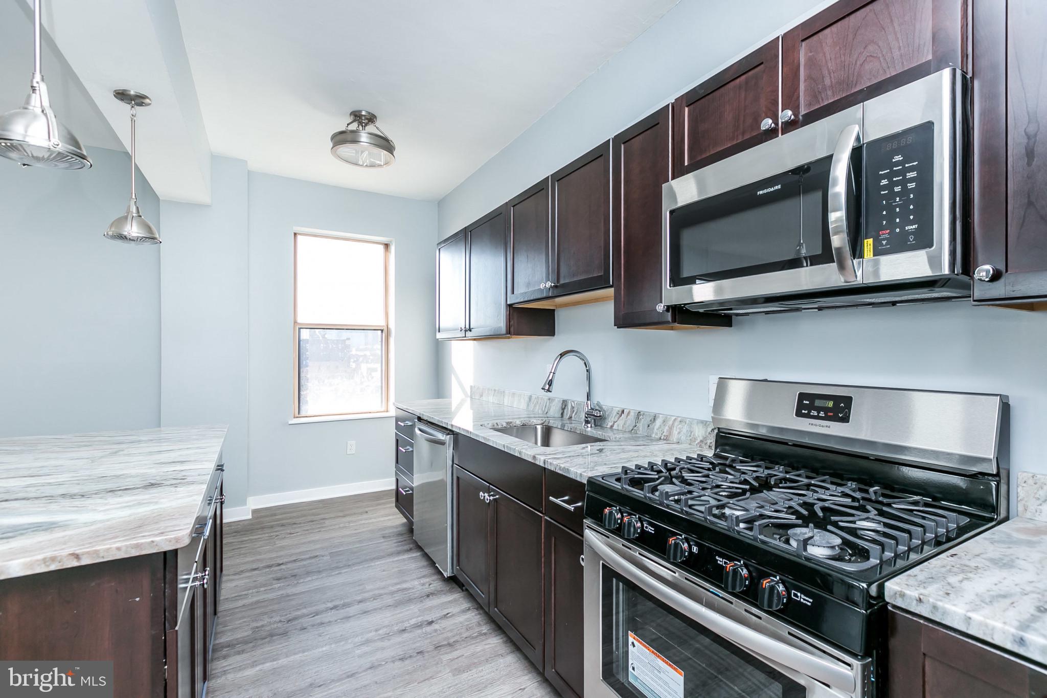 1001 St Paul Street, Unit 6G Baltimore, MD 21202 - Photo 12 of 32 a kitchen with stainless steel appliances a stove a microwave cabinets and a wooden floor