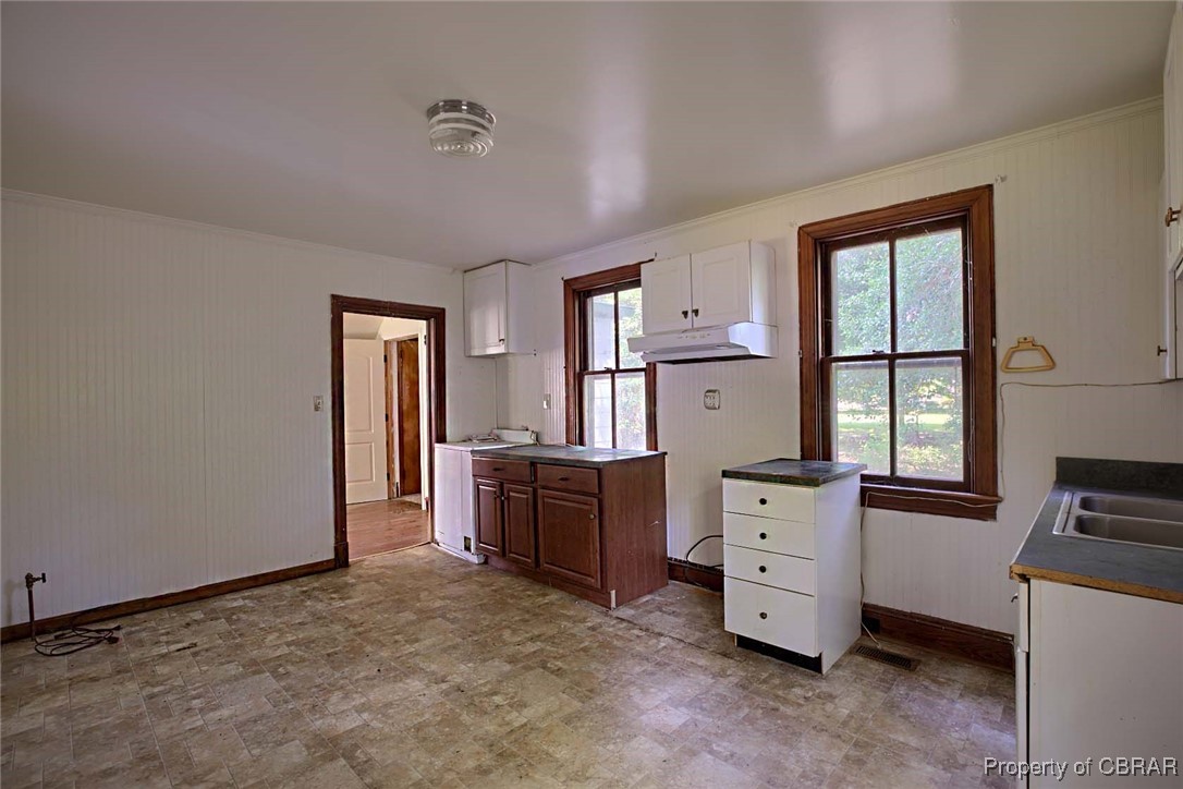 708 Calthrop Neck Road Yorktown, VA 23693 - Photo 17 of 24 Kitchen with under cabinet range hood, light floors, white cabinetry, ornamental molding, and wood walls