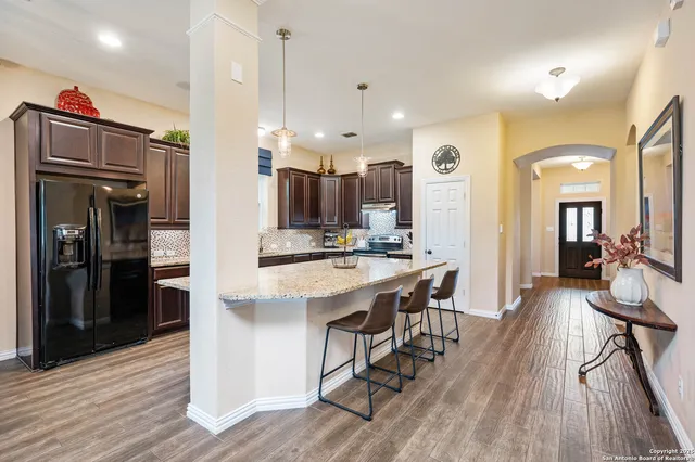 a kitchen with stainless steel appliances kitchen island granite countertop a refrigerator a stove a sink and a dining table with wooden floor
