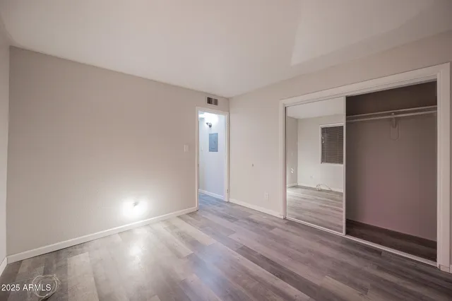 a view of an empty room with wooden floor & closet