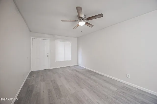 a view of an empty room with wooden floor and a ceiling fan