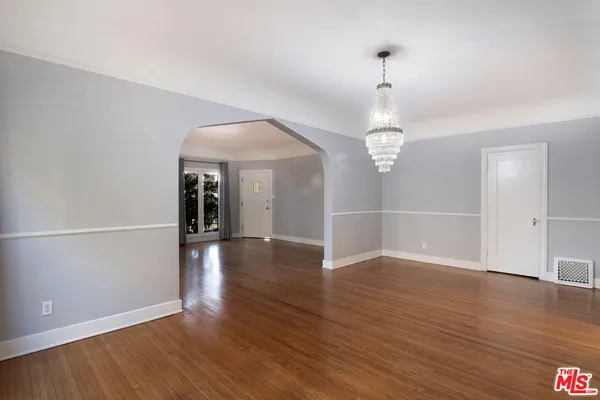 an empty room with wooden floor chandelier and windows