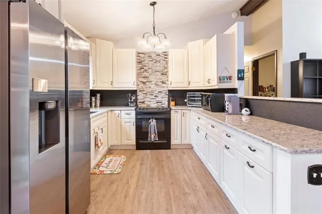 a kitchen with stainless steel appliances granite countertop a refrigerator a oven and white cabinets with wooden floors