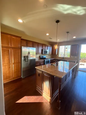 a kitchen with stainless steel appliances granite countertop a refrigerator a sink dishwasher a stove and a dining table with wooden floor