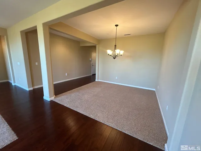 an empty room with wooden floor chandelier and hallway