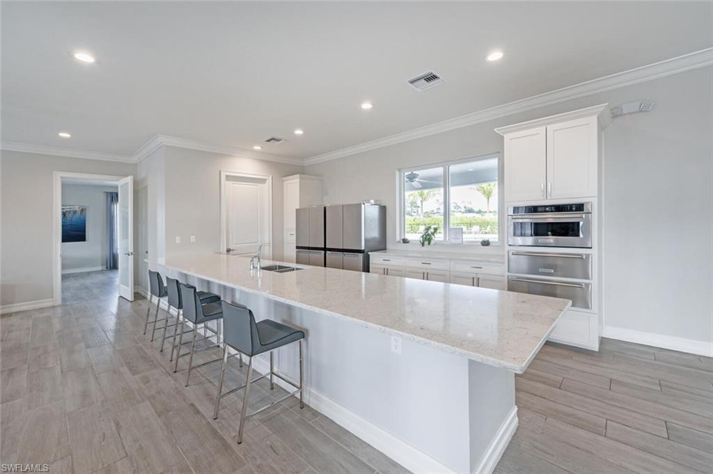 388 Grace Bay Lane Naples, FL 34114 - Photo 35 of 39 Kitchen featuring white cabinets, crown molding, a spacious island, light stone counters, and light wood-style flooring