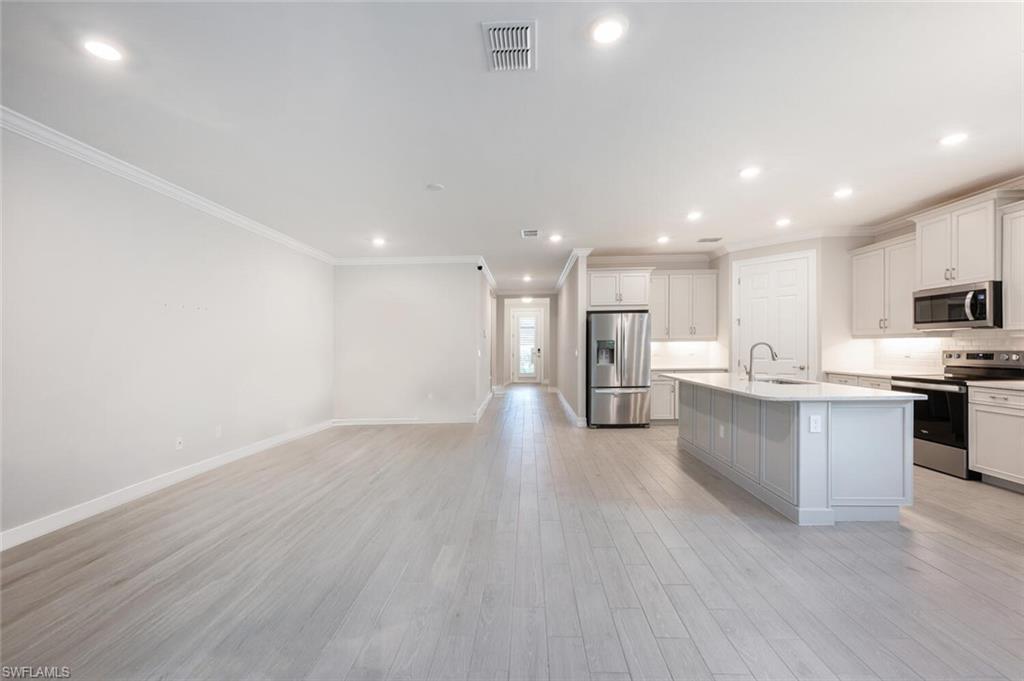 388 Grace Bay Lane Naples, FL 34114 - Photo 5 of 39 Kitchen with appliances with stainless steel finishes, white cabinets, recessed lighting, ornamental molding, and light wood finished floors