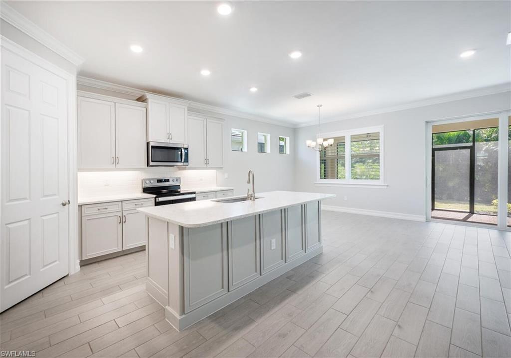388 Grace Bay Lane Naples, FL 34114 - Photo 6 of 39 Kitchen featuring crown molding, decorative backsplash, stainless steel appliances, an island with sink, and light wood-style flooring