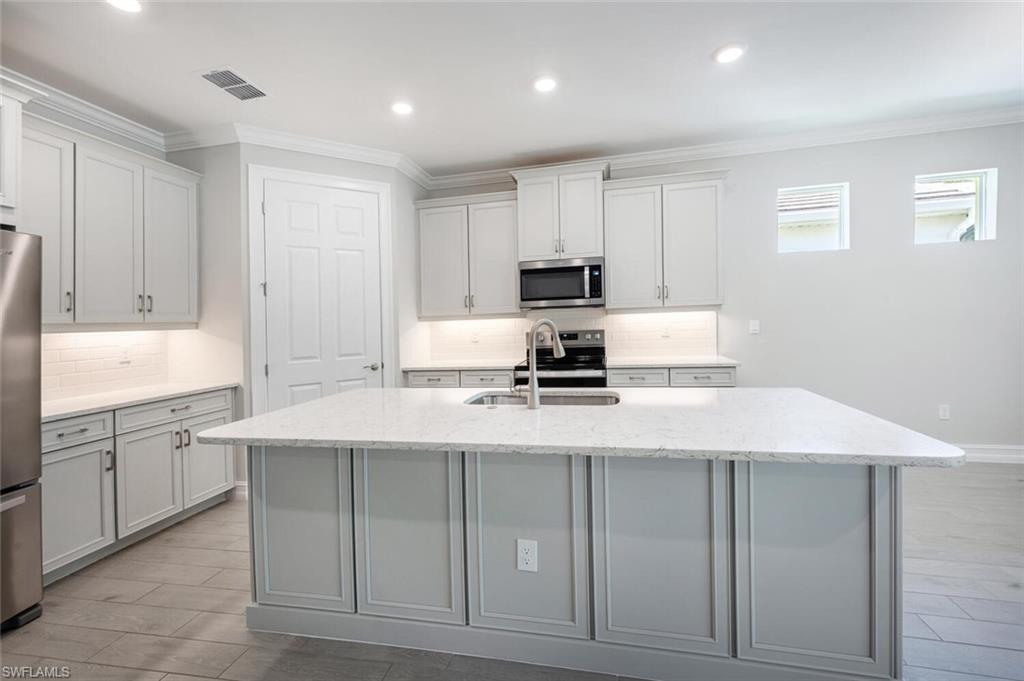 388 Grace Bay Lane Naples, FL 34114 - Photo 7 of 39 Kitchen featuring backsplash, ornamental molding, light stone counters, stainless steel appliances, and light wood-type flooring