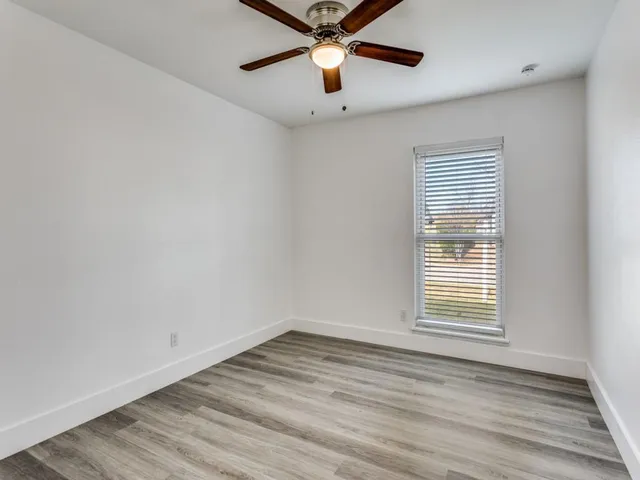 an empty room with wooden floor chandelier fan and windows