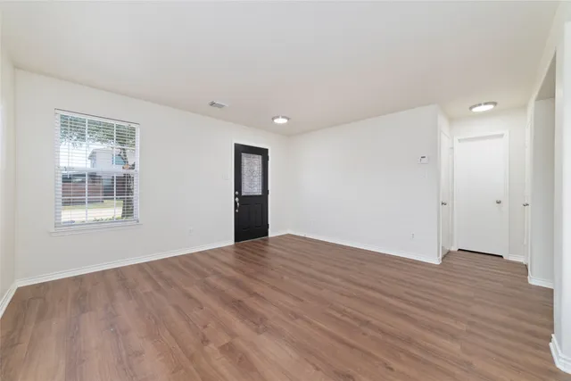 a view of an empty room with wooden floor and a window