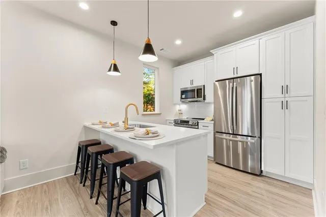 a kitchen with stainless steel appliances granite countertop a refrigerator a sink a stove a dining table and chairs with wooden floor