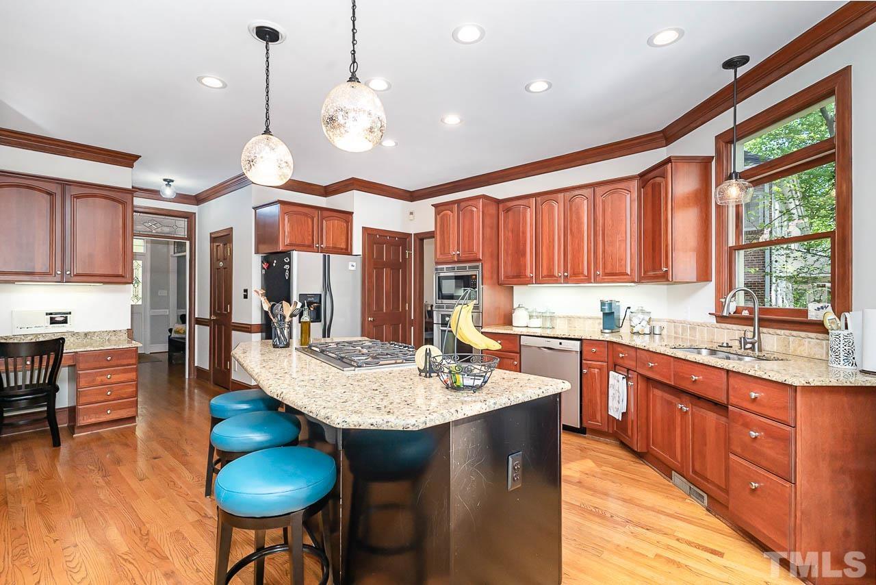 7512 Rainwater Road Raleigh, NC 27615 - Photo 23 of 45 a kitchen with stainless steel appliances granite countertop a stove top oven a dining table and chairs with wooden floor