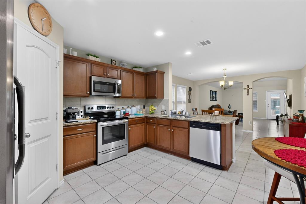 1409 Slate Street Princeton, TX 75407 - Photo 9 of 36 Spacious kitchen featuring wood cabinetry, stainless steel appliances, granite-style countertops, and tile flooring